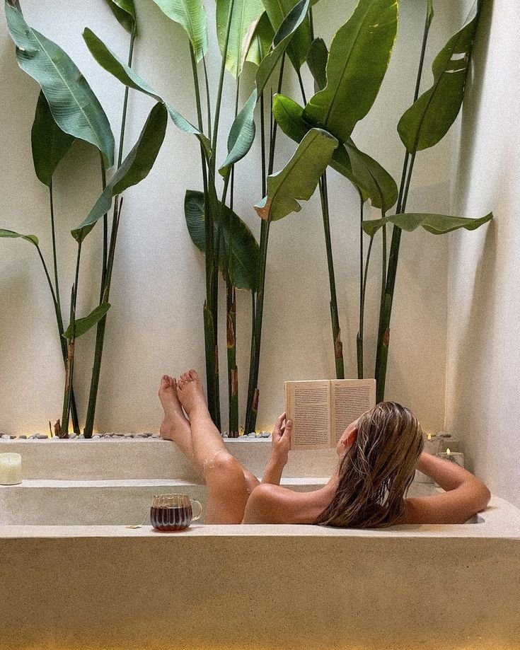 Woman reading in a stone bathtub beside tall banana plants
